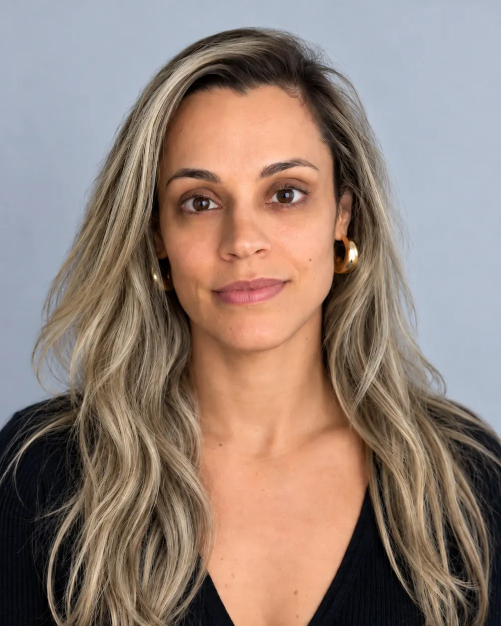 Mulher com cabelo longo loiro acinzentado e raiz escura, usando blusa preta sobre fundo cinza